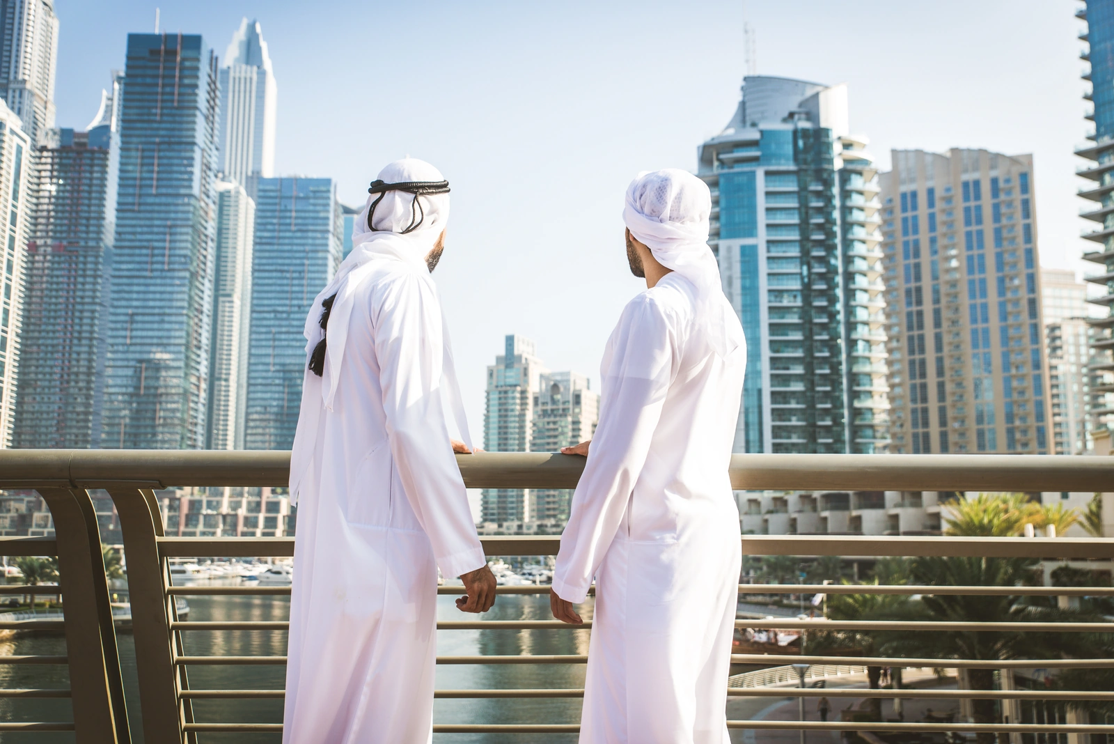 Two Emirati businessmen in kandora overlooking Dubai Marina — mainland business setup documents