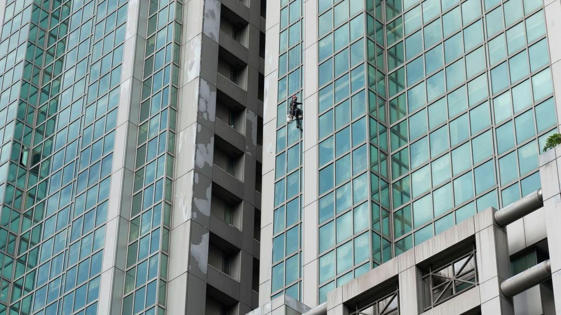 Rope access technician cleaning the glass facade of a high-rise tower