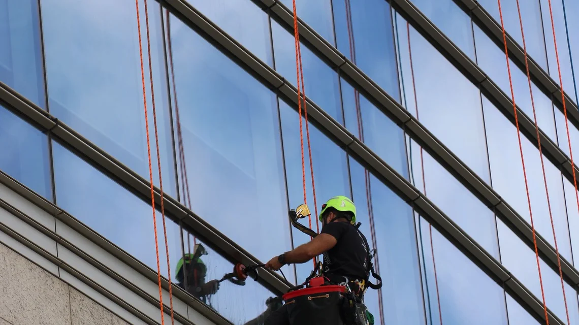 Cleaner abseiling down a glass office tower with cleaning equipment