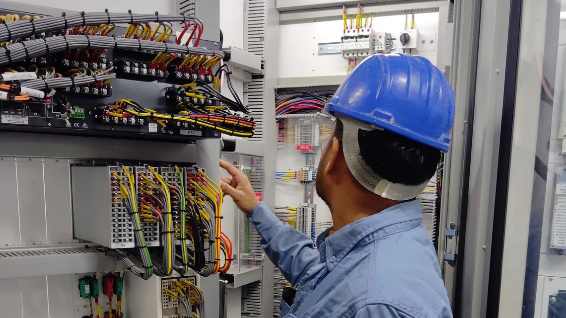 A technician in a hard hat working on a building switchgear panel in Dubai