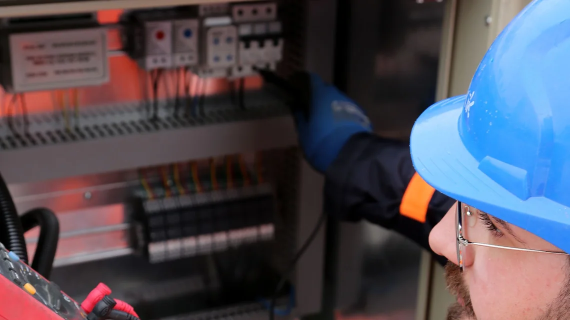 An electrician in full PPE testing a distribution board during building maintenance