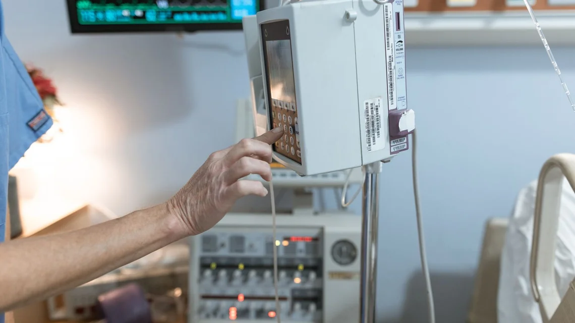 Medical staff operating an infusion pump beside a patient vital-signs monitor
