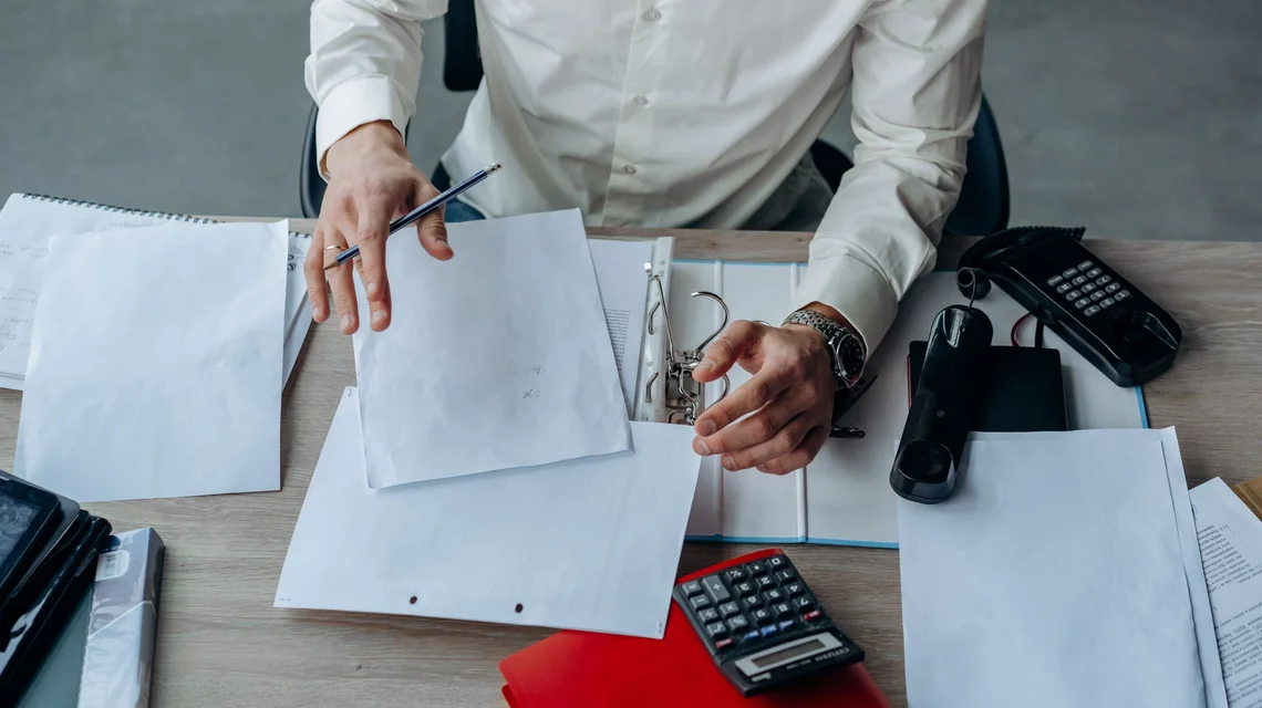 Person reviewing business paperwork and a calculator at a desk