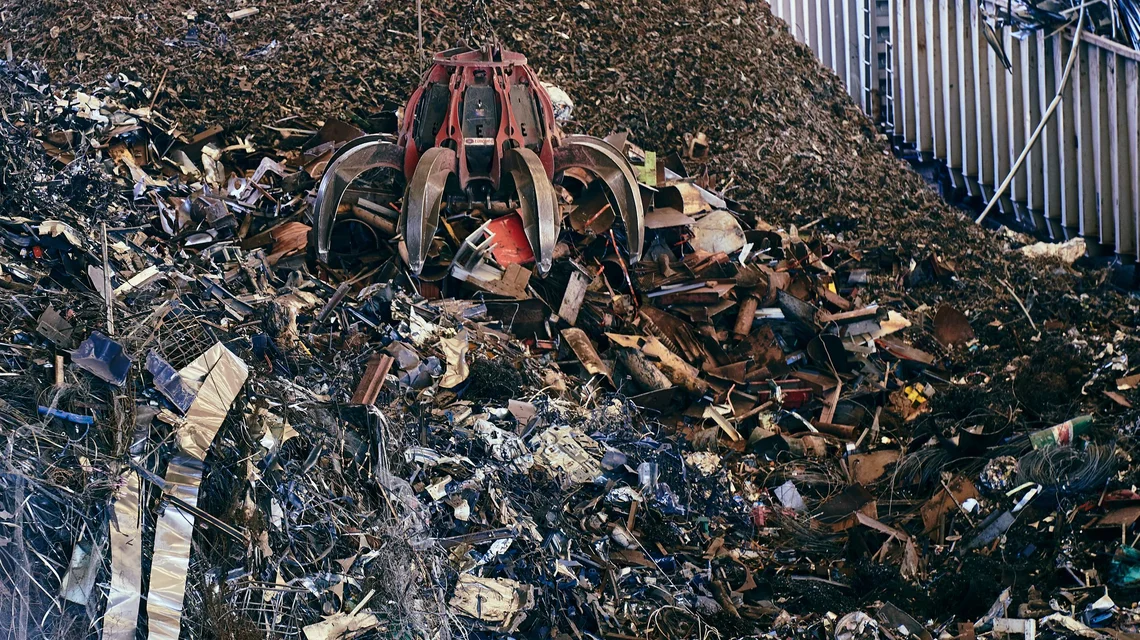 Grab crane working a pile of mixed scrap metal at a recycling yard